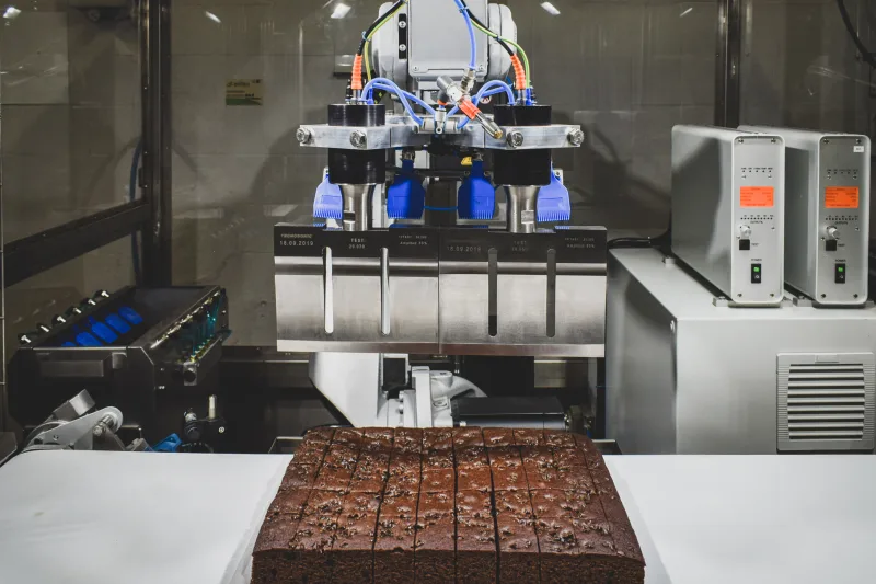 Cuchillas de ultrasonidos del robot de corte porcionando una plancha de bizcocho